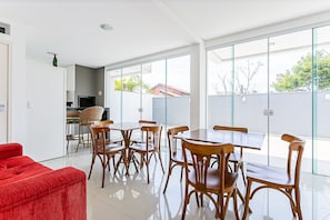 Un espace de repas moderne avec des tables et des chaises en bois, un canapé rouge et de grandes fenêtres donnant sur l’extérieur.