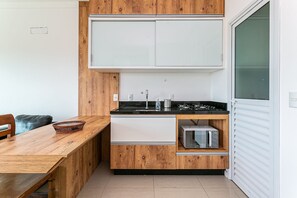 A compact kitchen with wooden cabinetry, a black countertop, and a built-in microwave. - New Studio 900 m From Lagoa da Conceicao - Ecm204 (Florianópolis)
