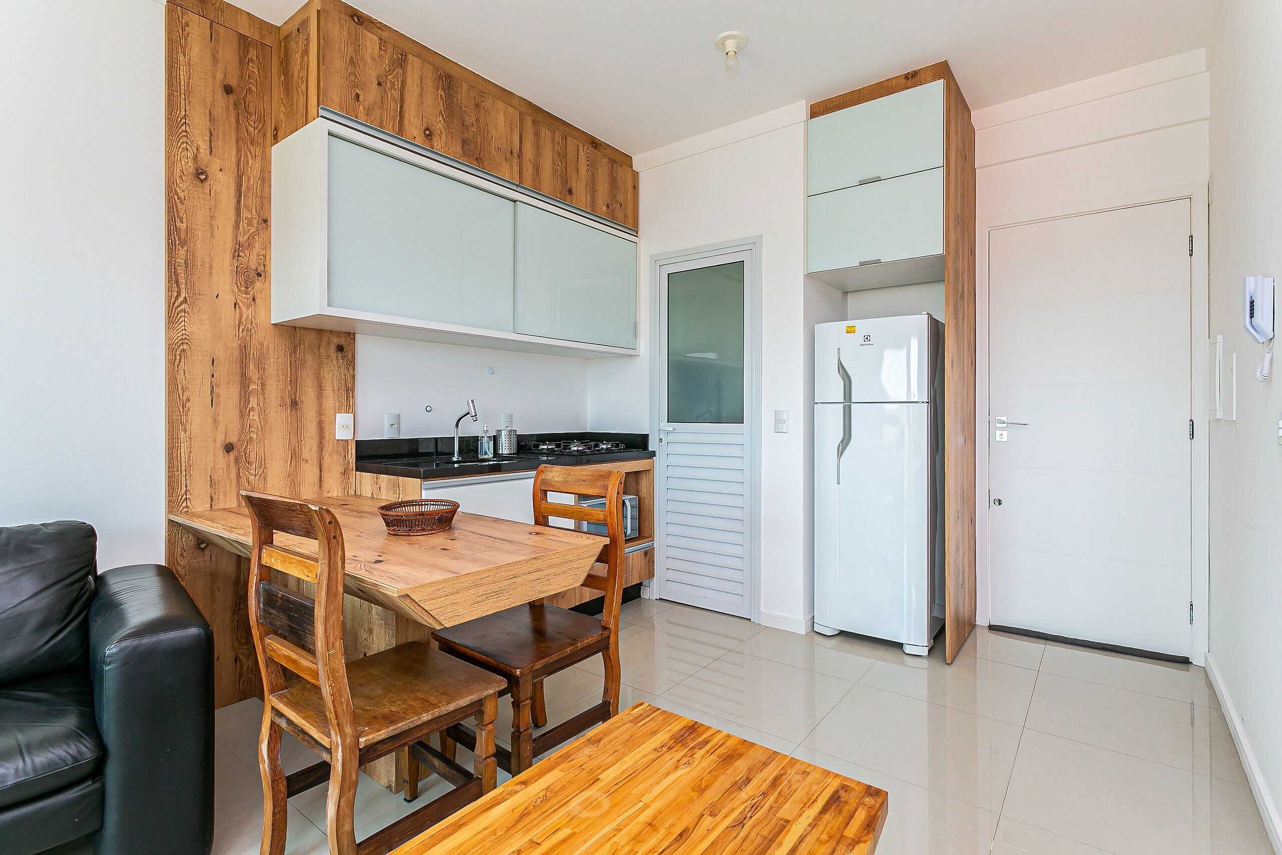 A modern kitchen with wooden cabinetry, a dining table with chairs, a refrigerator, and a white door.