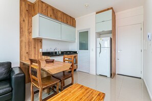 A modern kitchen with wooden cabinetry, a dining table with chairs, a refrigerator, and a white door. - New Studio 900 m From Lagoa da Conceicao - Ecm204 (Florianópolis)