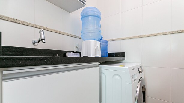 A compact laundry area with a washing machine, a water dispenser, and a faucet. - New Studio 900 m From Lagoa da Conceicao - Ecm204 (Florianópolis)