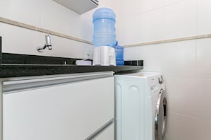 Ein kleiner Waschbereich mit Waschmaschine, Wasserspender und Wasserhahn.