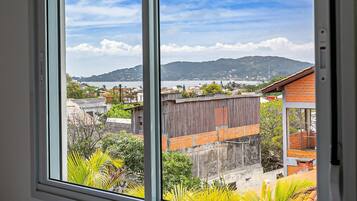 A view from a window overlooking a coastal area with buildings, greenery, and a distant mountain range.