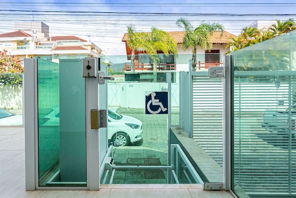 Entrada accesible en silla de ruedas con puerta de cristal, rampa y señal de estacionamiento.