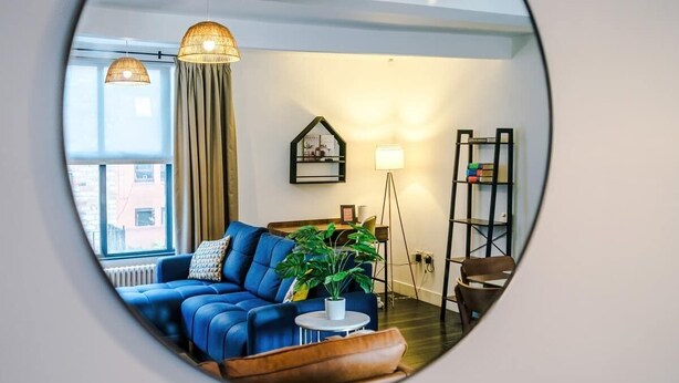 A circular mirror reflecting a living room with a blue sofa, a potted plant, a small table, and a bookshelf.