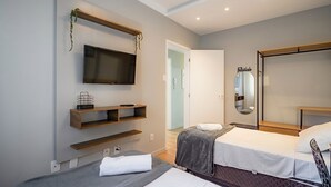 A hotel room with a TV mounted on the wall, a bed with a grey blanket, a bedside table, and a large mirror. - Charming Apartment in Downtown Floripa Edc402 (Florianópolis)