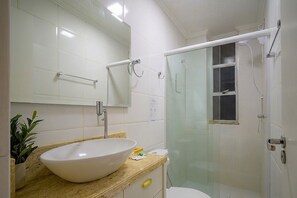 Une salle de bain avec un grand lavabo blanc, un miroir, une cabine de douche en verre et des toilettes.