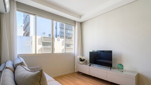 A modern living room with a sofa, a TV on a white console, and a large window. - Charming Apartment in Downtown Floripa Edc402 (Florianópolis)