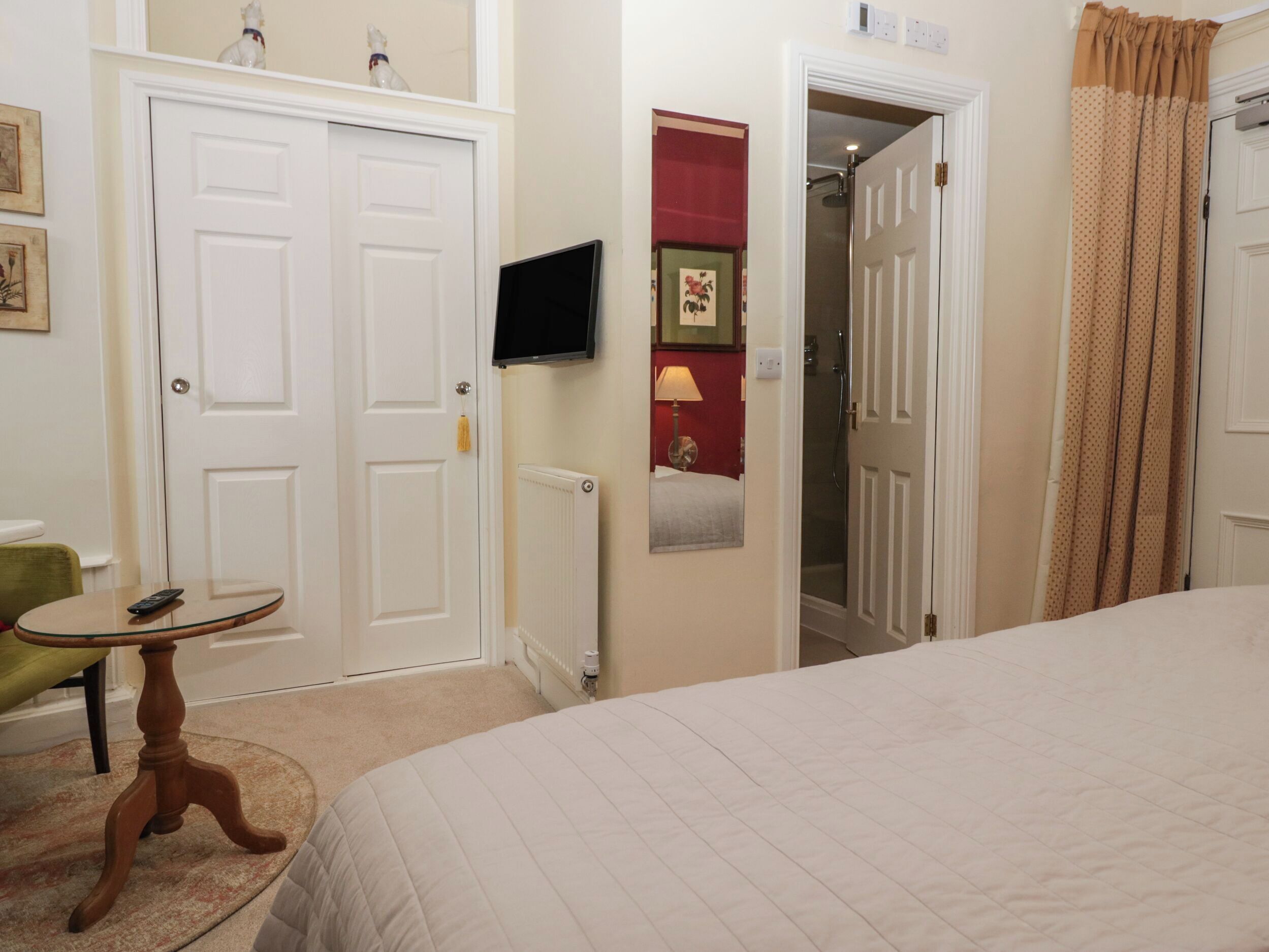 Una habitació d'hotel amb un llit, una televisió penjada a la paret, una taula rodona petita i una cadira.