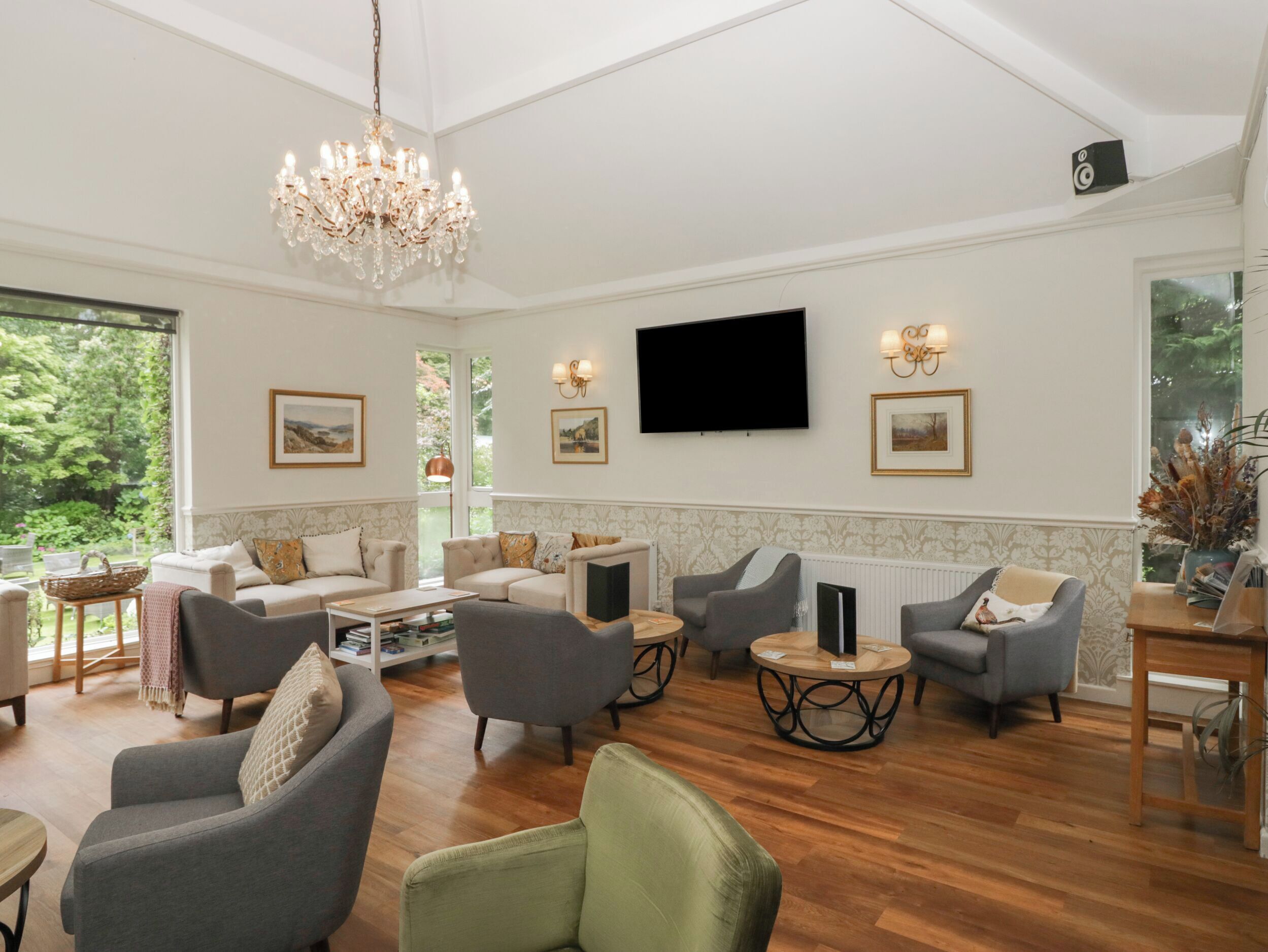 A spacious living area with multiple seating options, a chandelier, a flat-screen TV, and framed artwork on the walls.