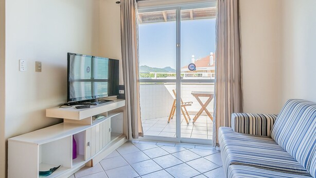 A living room with a TV on a white stand, a striped sofa, and a sliding glass door leading to an outdoor area with a table and chairs.