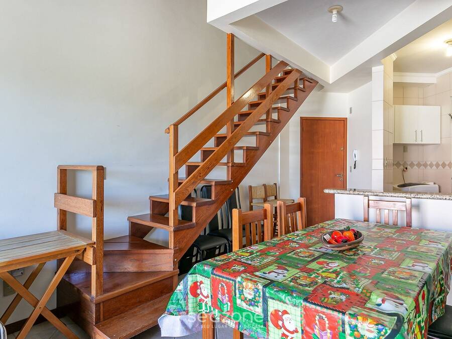 Un coin repas avec un escalier en bois, une table recouverte d’une nappe colorée et, au fond, une cuisine.