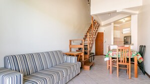 A living room with a striped sofa, a wooden staircase, and a dining area with a table and chairs.