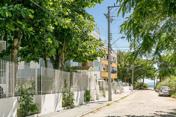 Una calle pavimentada bordeada de árboles y una valla blanca, que conduce a un edificio con balcones.