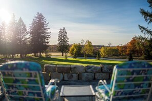Vista desde un patio con dos sillas y una mesa, que da a un área verde con árboles y una carretera.