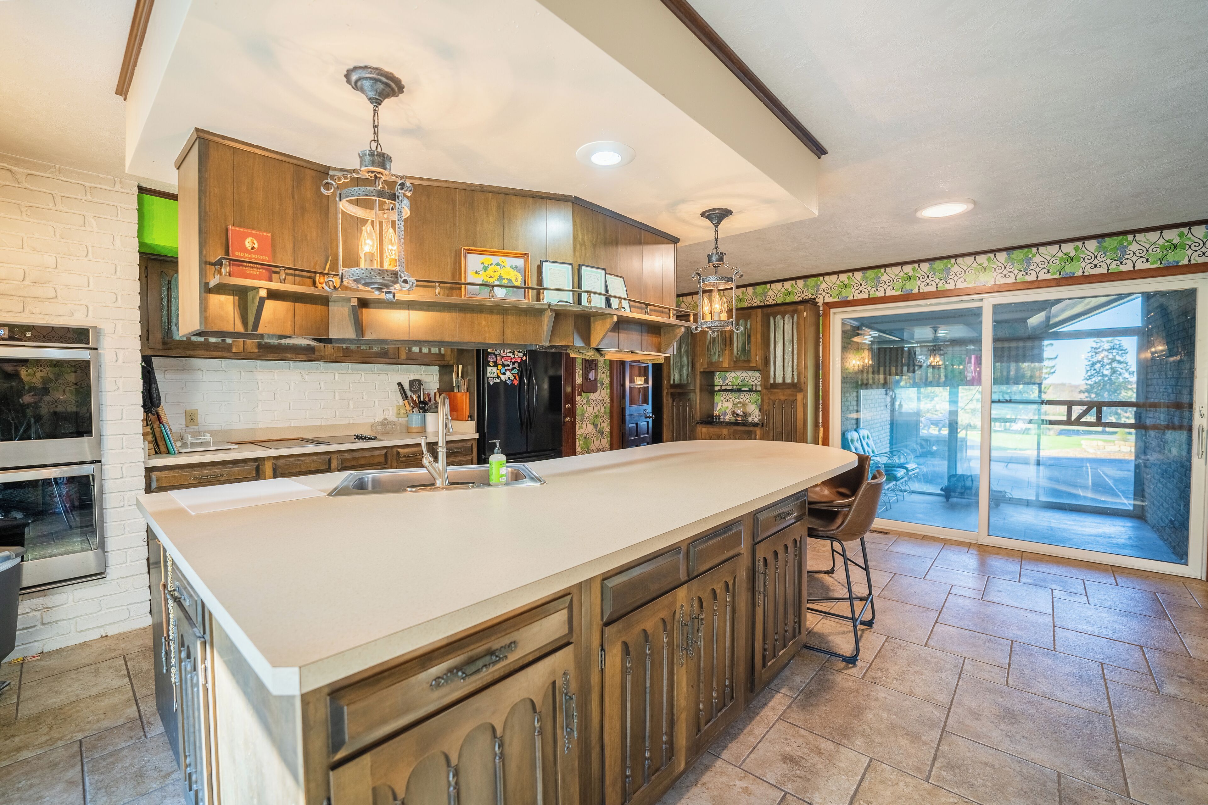 A spacious kitchen with a large island, wooden cabinets, and a view through the glass door.