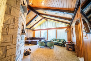 Una sala de estar acogedora con pared de piedra, vigas de madera en el techo, una chimenea, un sofá verde, una mesita de centro y una pequeña mesita auxiliar de madera.