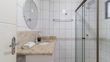 A bathroom with a marble sink, a mirror, a towel, and a glass shower enclosure.