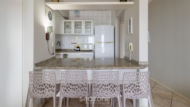 A kitchen with white cabinets, a granite countertop, and a white refrigerator. There are four white chairs with a unique design. - Charming Apt With Balcony and Sea View Edj0410 (Florianópolis)