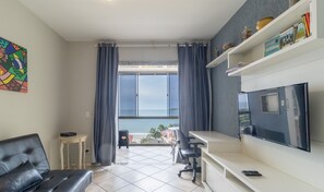 A modern living room with a large TV, a sofa, a small table, and a view of the sea through large windows. - Charming Apt With Balcony and Sea View Edj0410 (Florianópolis)