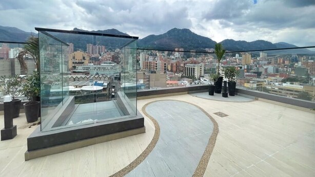 A rooftop terrace with a glass balustrade, potted plants, and a cityscape view. - City-view apartment in Chapinero – fast WiFi, 24h security, gym & coworking (Bogotá)