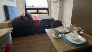 A hotel room with a bed, a TV mounted on the wall, a dining table set with plates, glasses, and a cup, and a window with a cityscape view. - City-view apartment in Chapinero – fast WiFi, 24h security, gym & coworking (Bogotá)