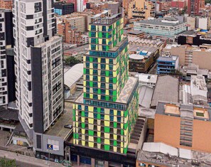 Un edificio de varios pisos con una fachada inusual a cuadros, rodeado de otras construcciones urbanas.