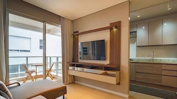 A modern apartment with a balcony, a dining area, a kitchen, and a mounted TV. - Apt Close to Beach & Floripa Shopping [eaz305] (Florianópolis)