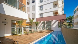 A swimming pool area with a wooden deck, lounge chairs, and a sign indicating an emergency pool. - Apt Close to Beach & Floripa Shopping [eaz305] (Florianópolis)