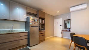A compact kitchen with a refrigerator, wooden cabinets, a microwave, and a dining area with chairs and a table. - Apt Close to Beach & Floripa Shopping [eaz305] (Florianópolis)