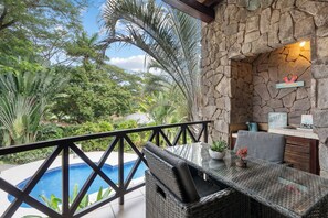 A poolside area with wicker furniture, a stone wall, and lush greenery. - Modern Island-Themed Condo with Floor-to-Ceiling Windows & Garden and Pool Views Within Walking Distance of the Beach (Sardinal)