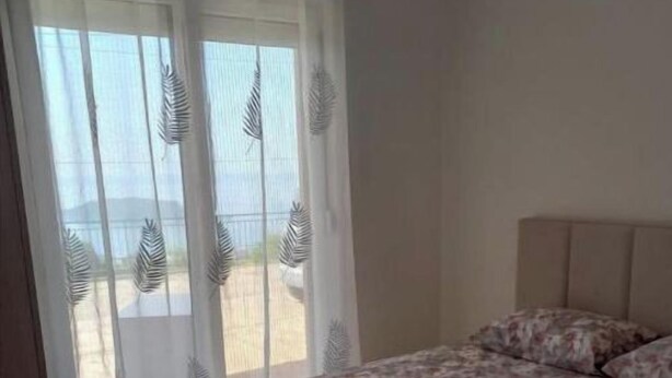 A bedroom with a bed, a window with sheer curtains, and a view of the outdoors.