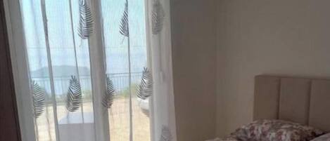 Un dormitorio con cama, una ventana con cortinas translúcidas y vistas al exterior.