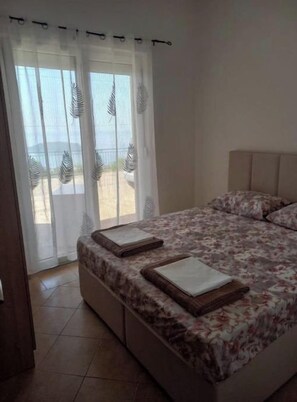 Un dormitorio con cama, una ventana con cortinas translúcidas y vistas al exterior.