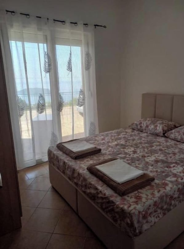 Un dormitorio con cama, una ventana con cortinas translúcidas y vistas al exterior.