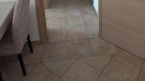 Un couloir étroit au sol carrelé, un bureau avec une chaise et une porte sur le côté droit.