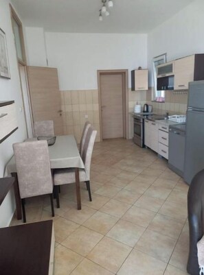 A compact kitchen with a dining table, chairs, and basic appliances. - Apartman Vujović1 (Budva)