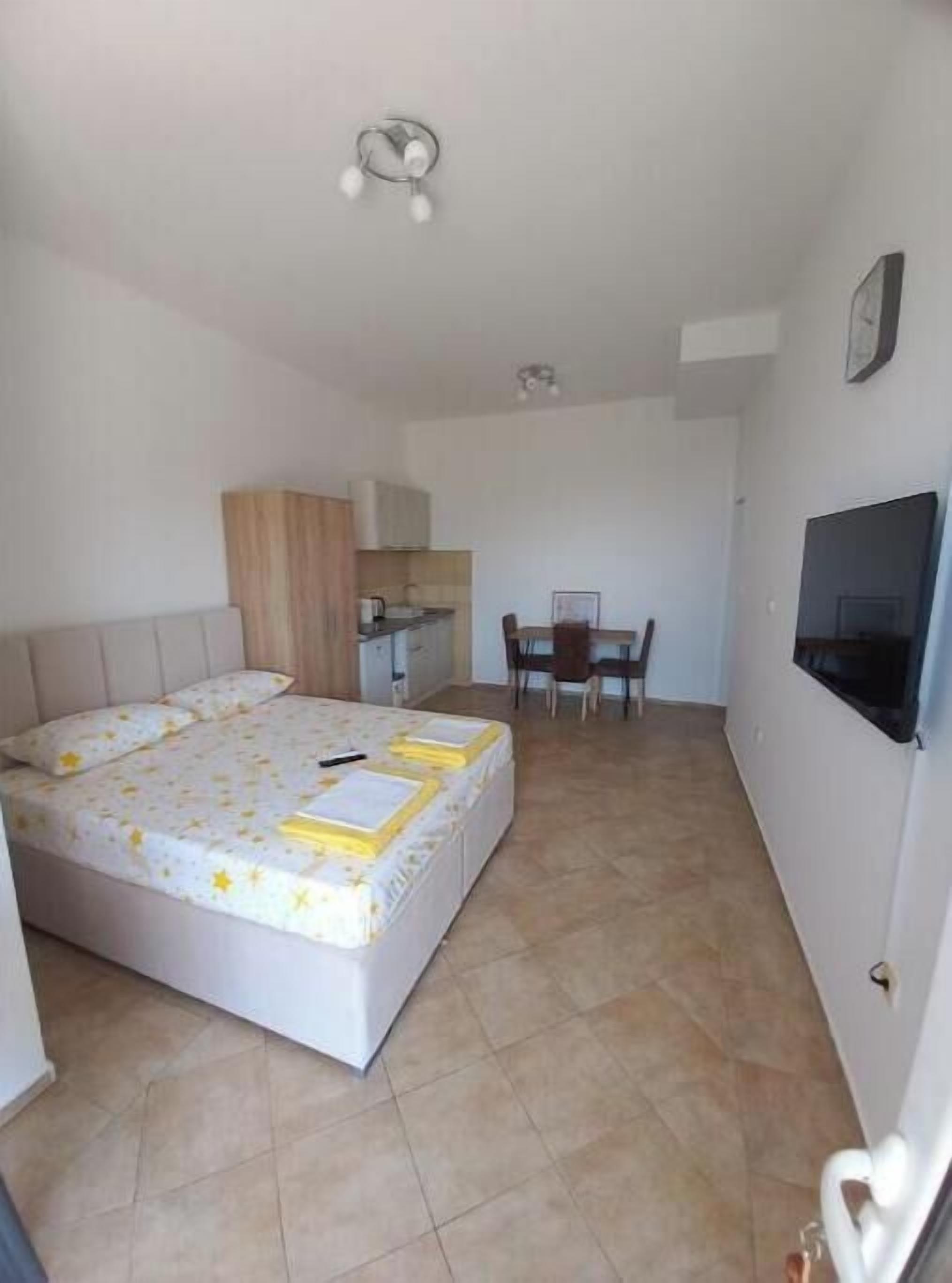 A bedroom with a bed, a small kitchenette, a dining area, and a TV.