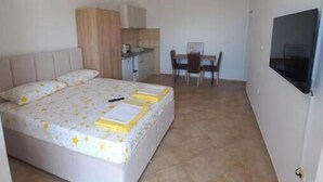 A bedroom with a bed, a small kitchenette, a dining area, and a TV.