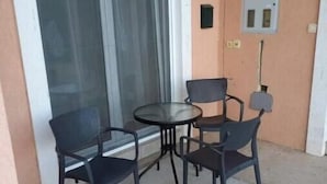 A small outdoor seating area with a table and four chairs, a sliding glass door, and a power outlet on the wall.