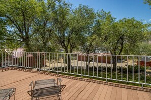 A wooden deck with metal chairs, surrounded by a white metal fence, and trees in the background.