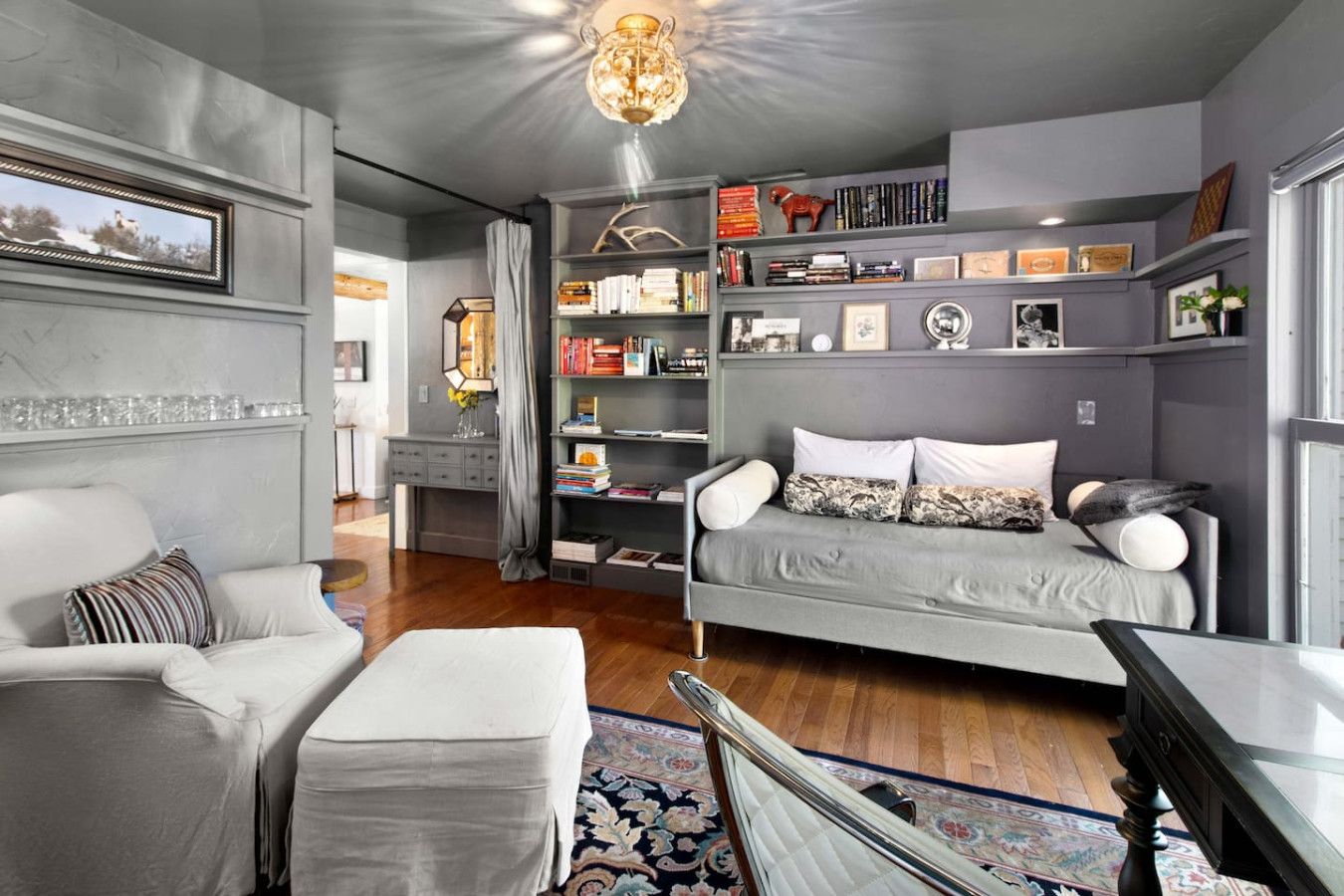 A modern living room with a grey sofa, a white armchair, and a wooden coffee table. There is a bookshelf filled with books and decorative items.