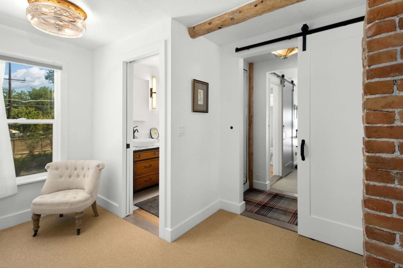 Quarto com uma janela grande, uma cadeira, cômoda de madeira e uma porta deslizante para um banheiro.