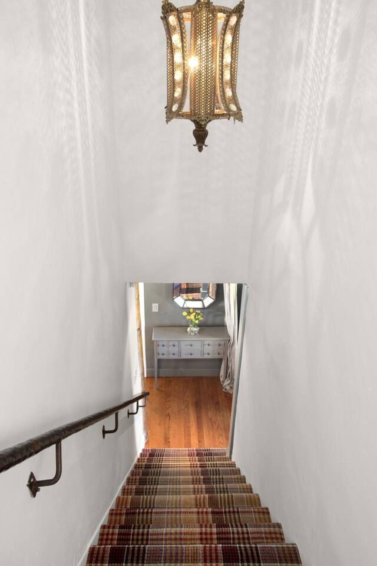 Un escalier recouvert d’une moquette à carreaux mène à une pièce où se trouve une coiffeuse et un miroir au-dessus.