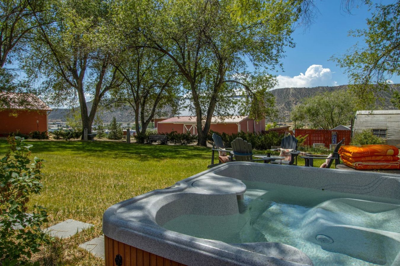 A hot tub in a backyard with a lawn, trees, and a mountain in the background.