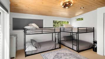 Une chambre avec des lits superposés, un plafond en bois, une fenêtre donnant sur un paysage verdoyant et un tapis à motifs sur le sol.