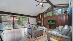 Ein geräumiges Wohnzimmer mit Kamin, Fernseher und einer großen Schiebetür, die auf eine Terrasse im Freien führt.