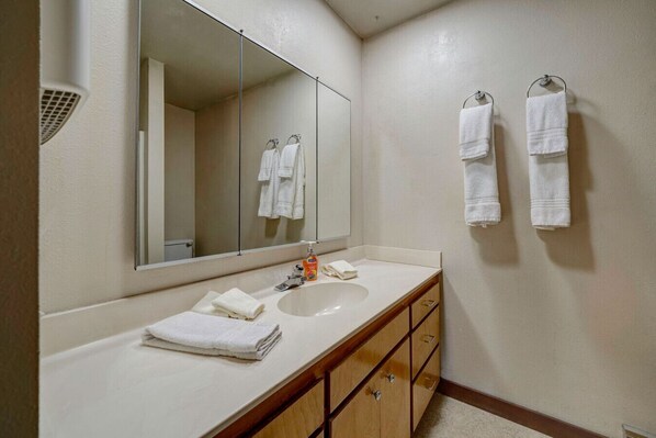 Un baño con lavamanos blanco, un espejo y dos toalleros con toallas blancas.