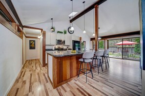 Una cocina moderna con una isla de madera, taburetes de bar y un amplio ventanal con vistas a un patio.