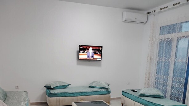 A modern bedroom with two beds, a sofa, a coffee table, and a TV mounted on the wall.